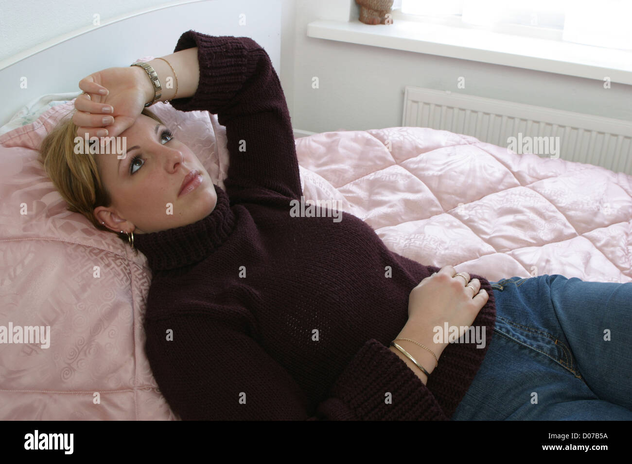 Young woman on bed with headache and stomach cramps staring at the