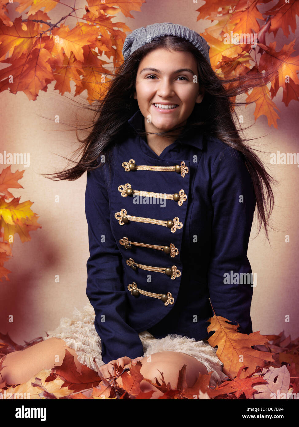 Smiling teenage girl sitting on fallen autumn leaves artistic fall fashion portrait Stock Photo
