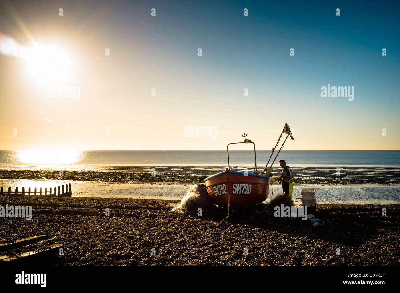 A local fisherman un-packs and tidies his nets in the early morning sun on Worthing Beach Stock Photo