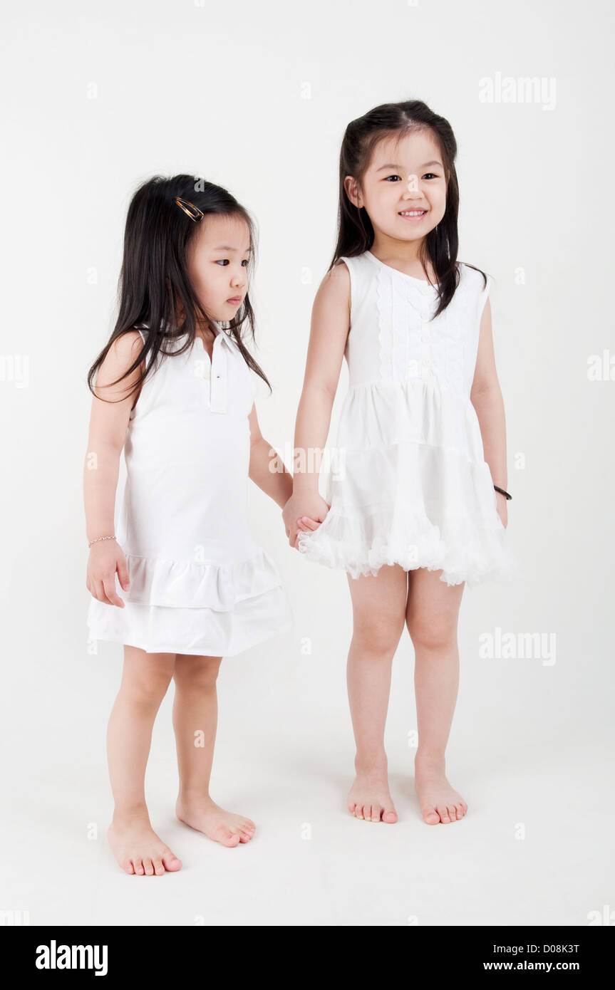 Asian sisters holding hand on plain background Stock Photo