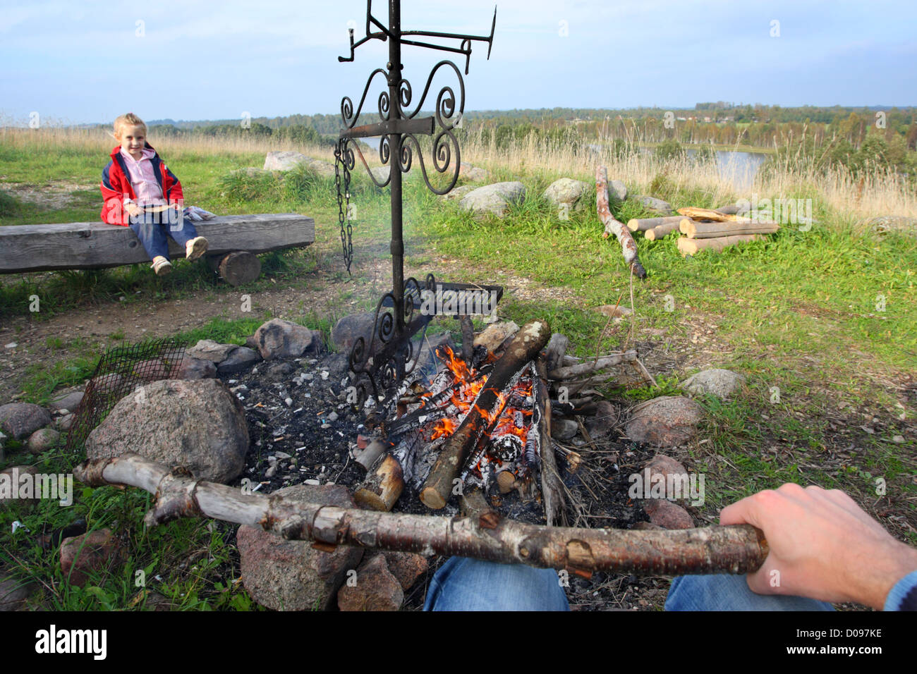 Dad sitting with his child around the open fire, getting ready for outdoor cooking. Stock Photo