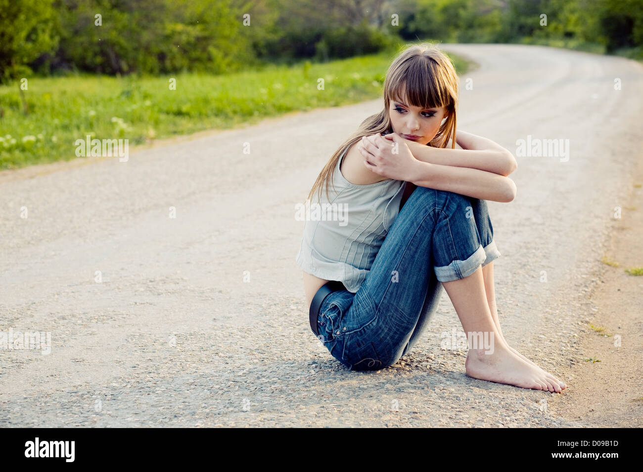 Sad girl sitting down on road Stock Photo - Alamy