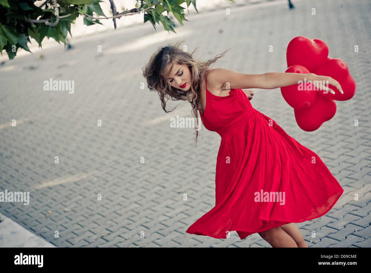 Beautiful girl in red dress moving with ballons as hearts Stock Photo