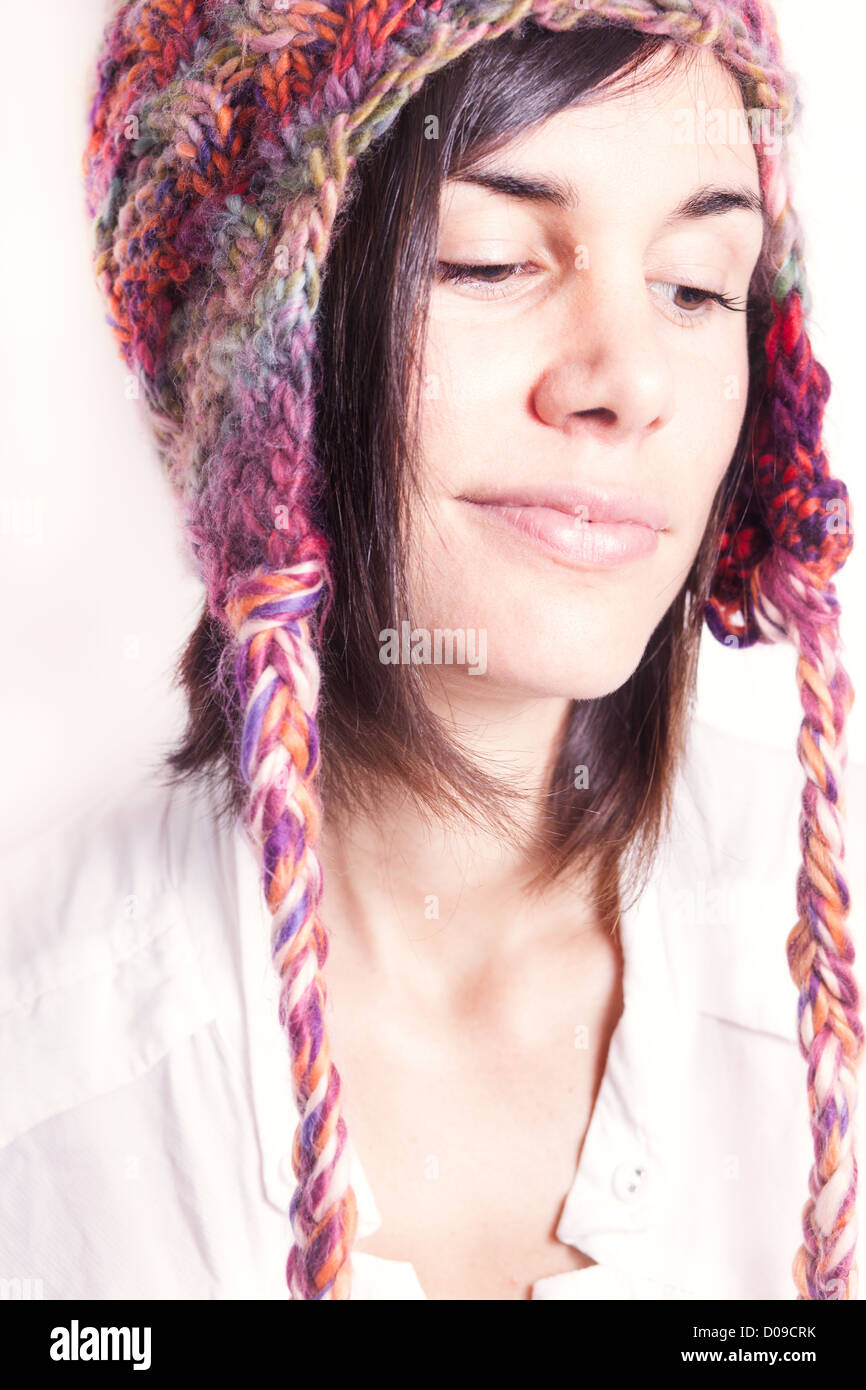 Young woman wearing woolly hat smiling to herself against white