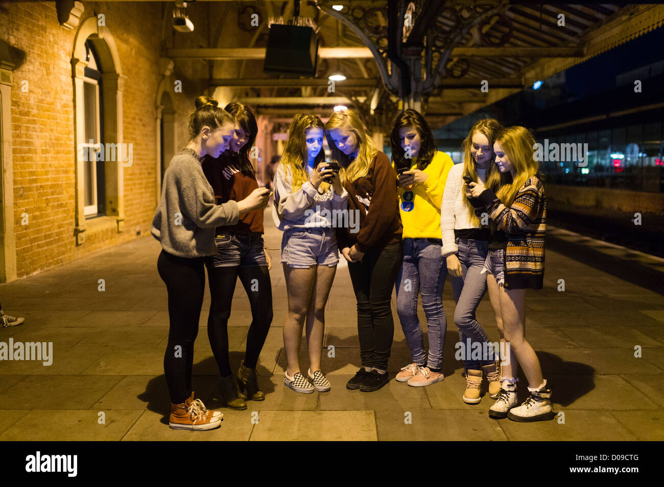 A group of seven 14 15 year old teenage girls friends together outside texting messages on their mobile phones at night UK Stock Photo