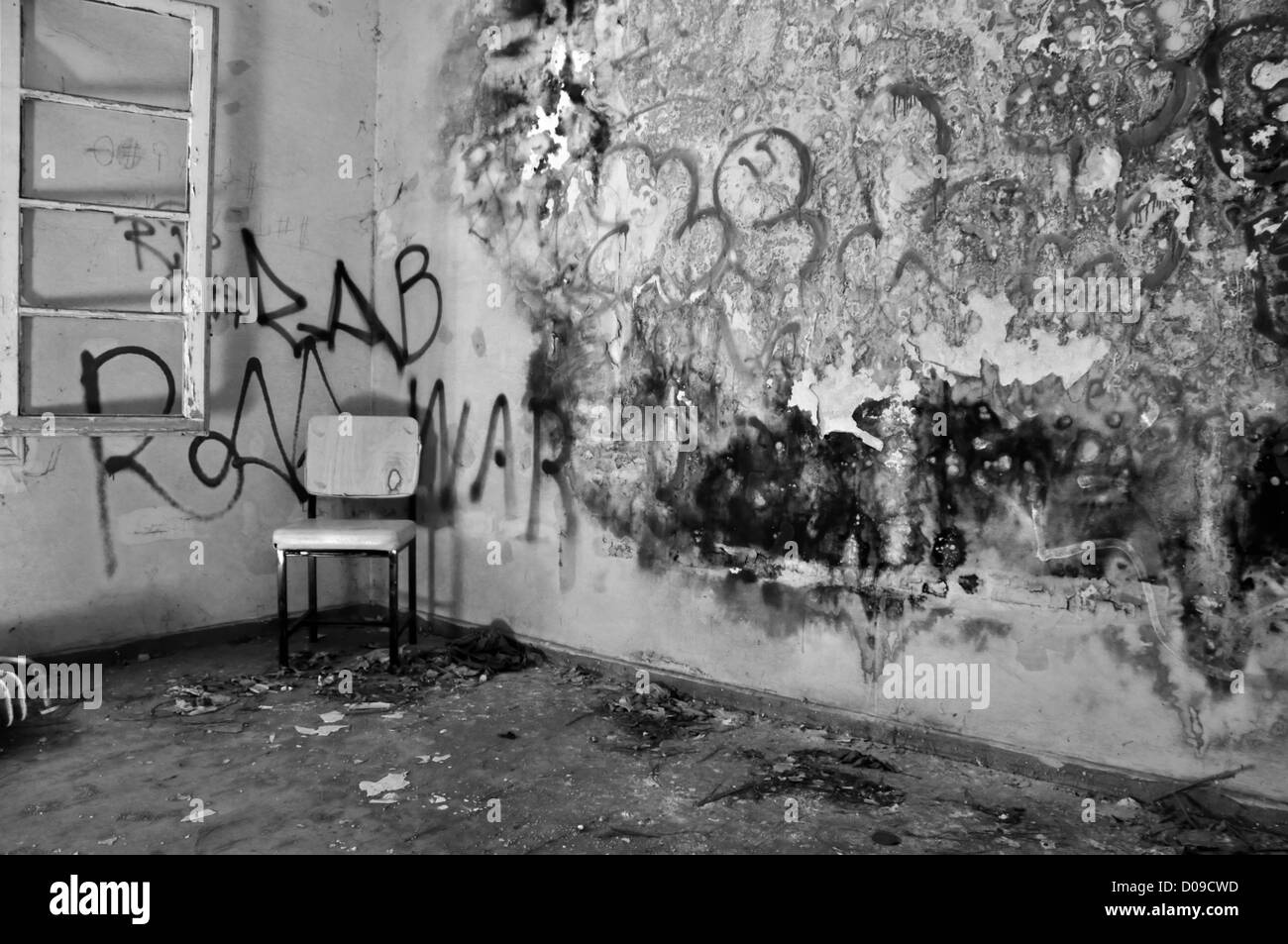Chair in the corner of a decayed room with peeling moldy wall. Black and white. Stock Photo