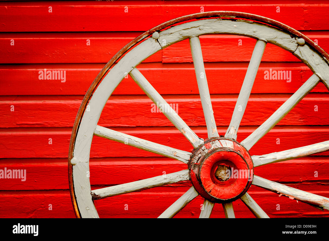 Old weathered wagon wheel leaning against painted red wall Stock Photo