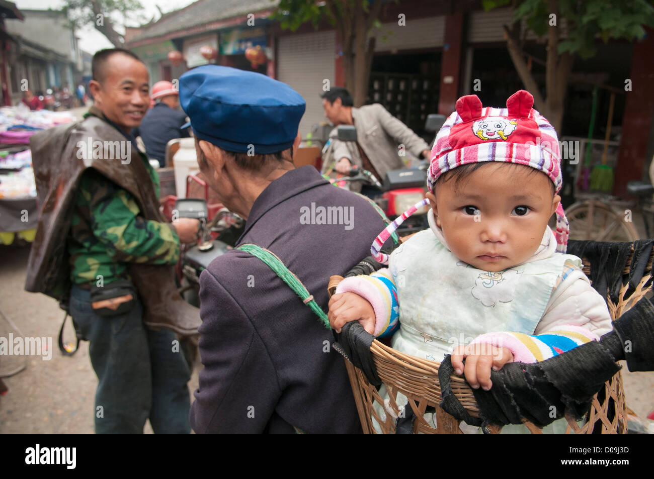 Baby boy is carried in basket by grandfather on busy market day in