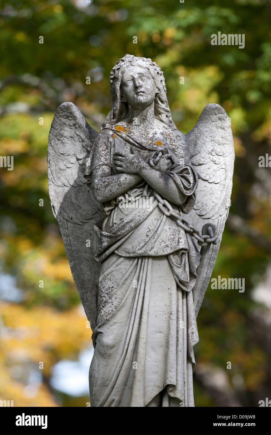 A sad angel with wings and arms folded against her chest looking upwards with a chain in hand. Stock Photo