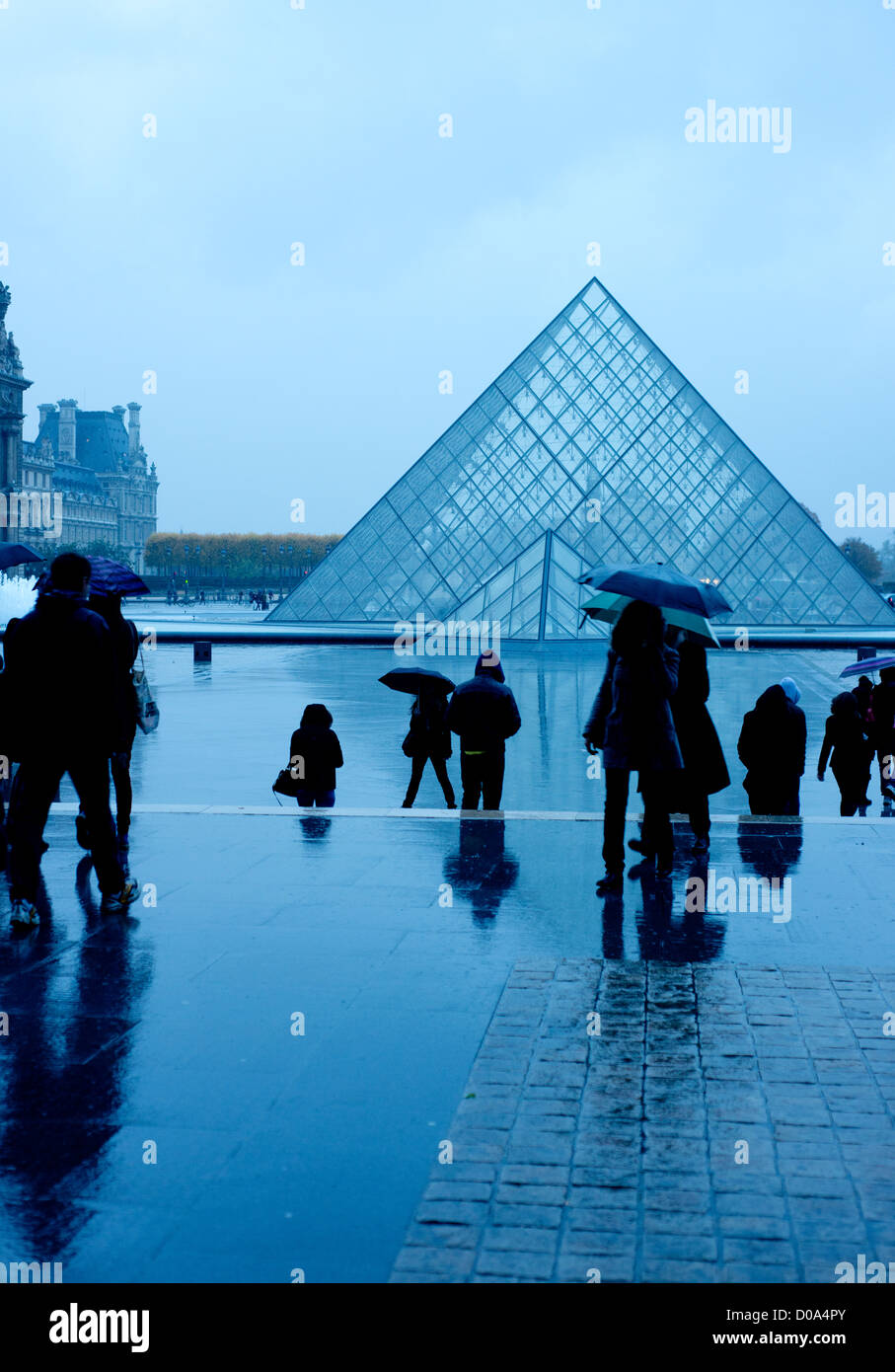 The Louvre pyramid on a wet autumn evening with people rushing home Stock Photo