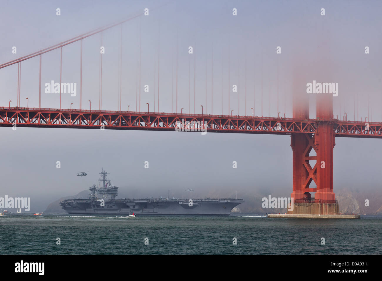 Aircraft carrier USS Carl Vinson passes slowly under the Golden Gate Bridge during Fleet Week as helicopter hovers in background Stock Photo