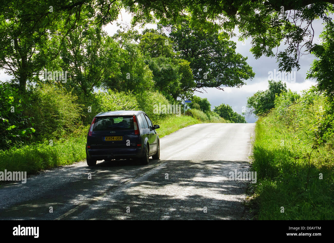 A car driving up a hill on a country lane through trees on a sunny day. Stock Photo