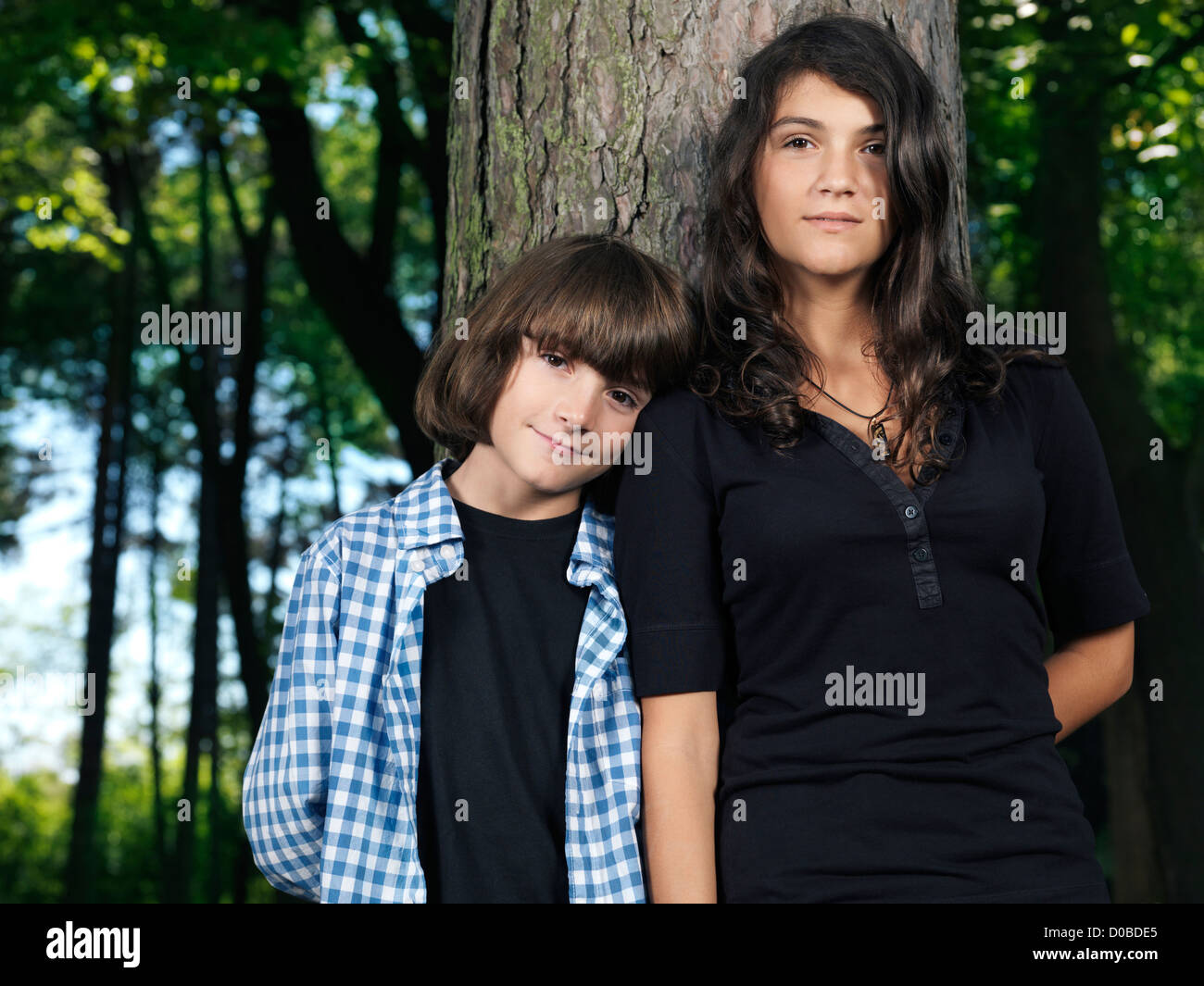 Emotional portrait of a teenage sister and a younger brother standing together leaning against a