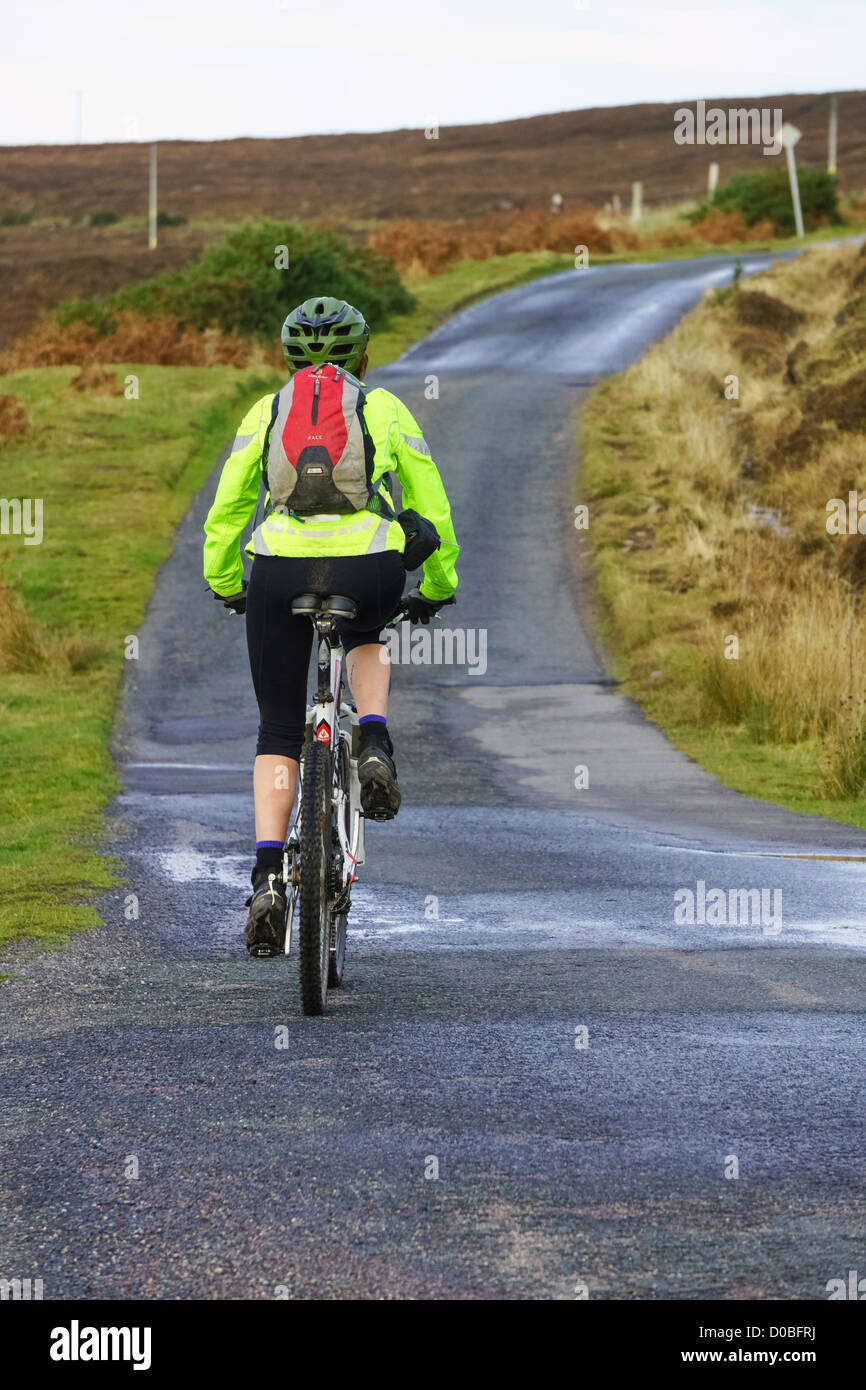 A woman bike rider peddling up a hill in the Scottish Highlands. Stock Photo