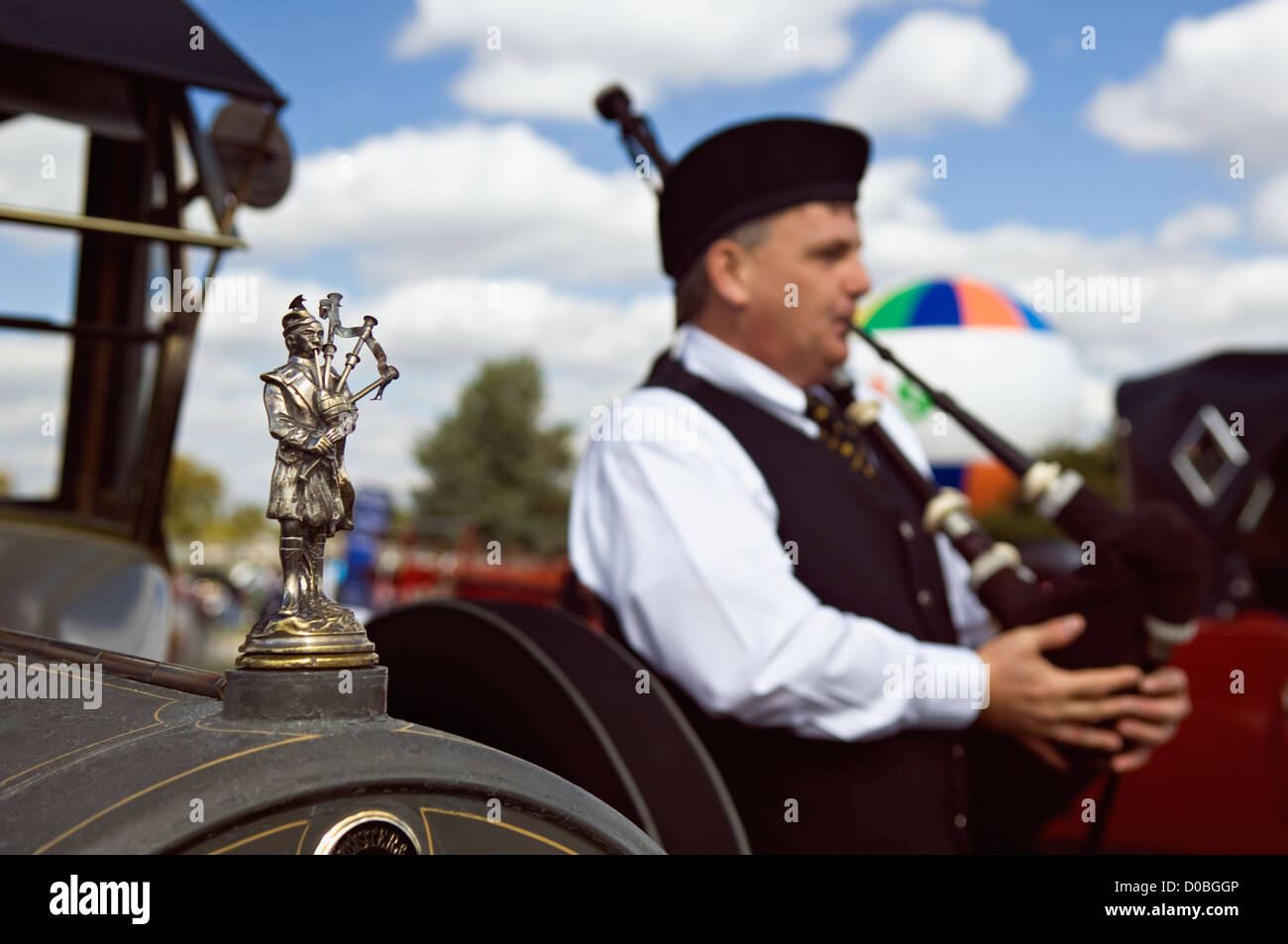Bagpiper Hood Ornament on Antique Car with Real Bagpiper in the Background Stock Photo