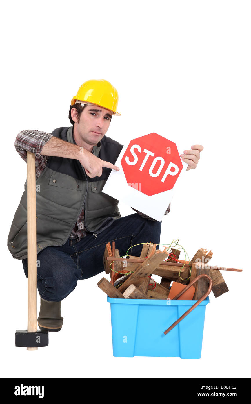 Labourer holding a stop sign while squatting before a bin full of wood ...