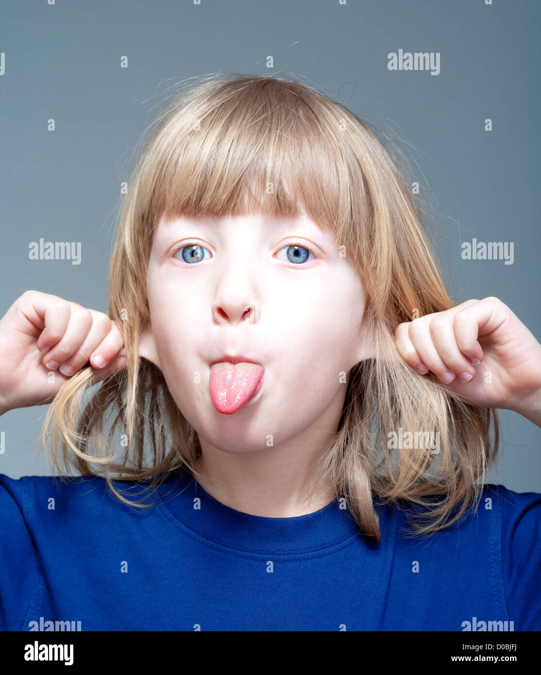 boy with long blond hair sticking out his tongue and pulling ears Stock Photo Alamy