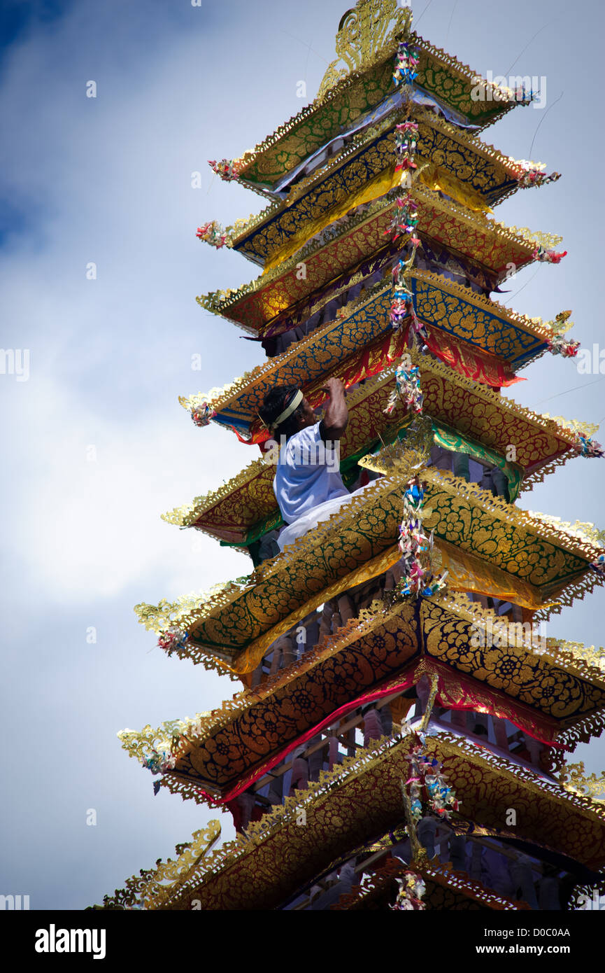 One person climbs up the tower where the deceased King of Ubud is waiting to be taken to the cremation area with the offers Stock Photo