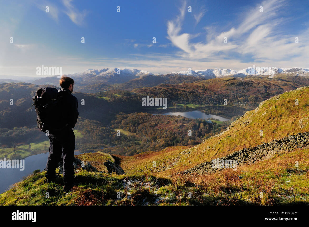 Walker admiring view from Nab Scar in the English Lake District. Rydal Water, Grasmere and snow covered fells in the distance Stock Photo