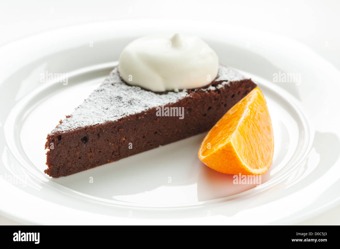 Chocolate truffle cake topped with cream with piece of orange Stock