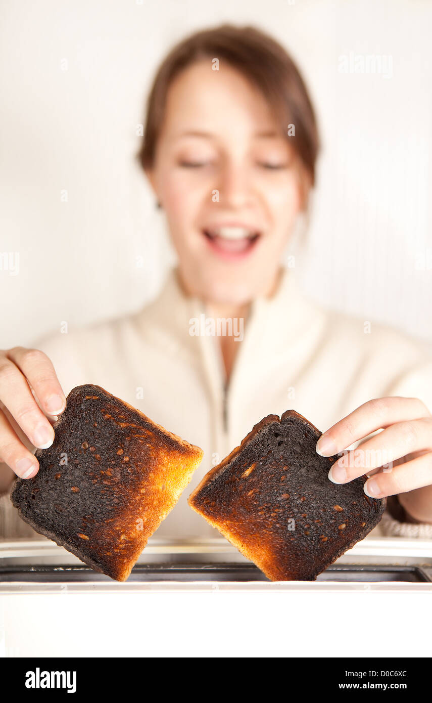 Surprised woman taking burnt toast out of a toaster Stock Photo