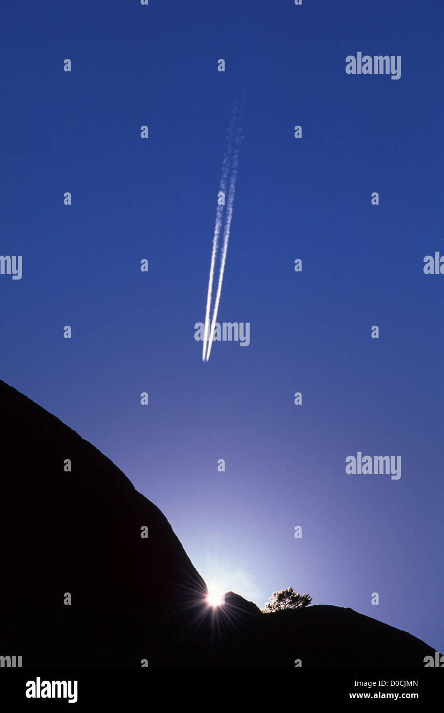 The Sun's Rays Diffract Over A Granite Cliff As A Passenger Jet Cuts Through The Cobalt Sky Above Stock Photo