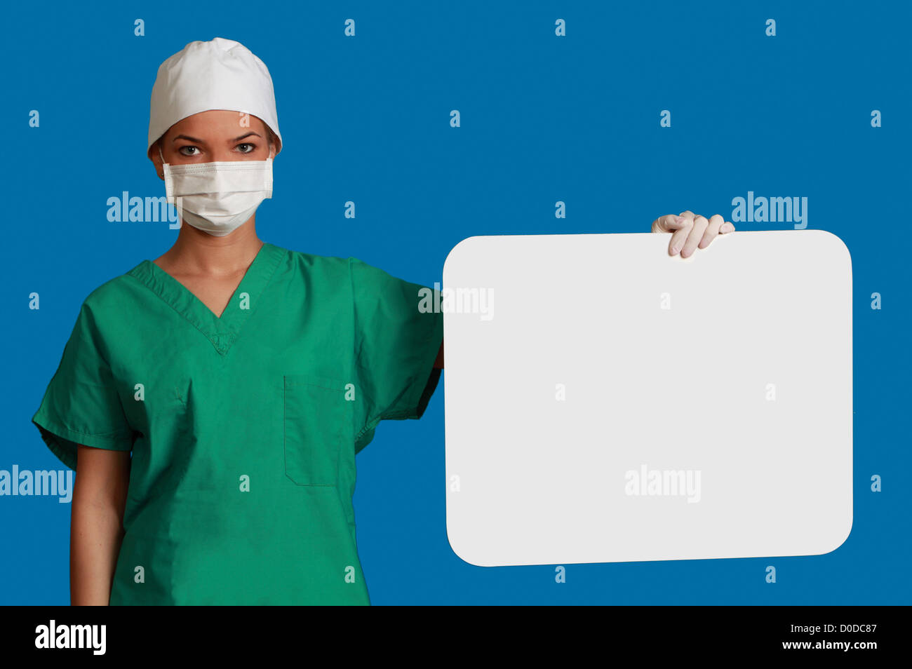 A young woman doctor holding an empty white bill board against a blue background. Stock Photo