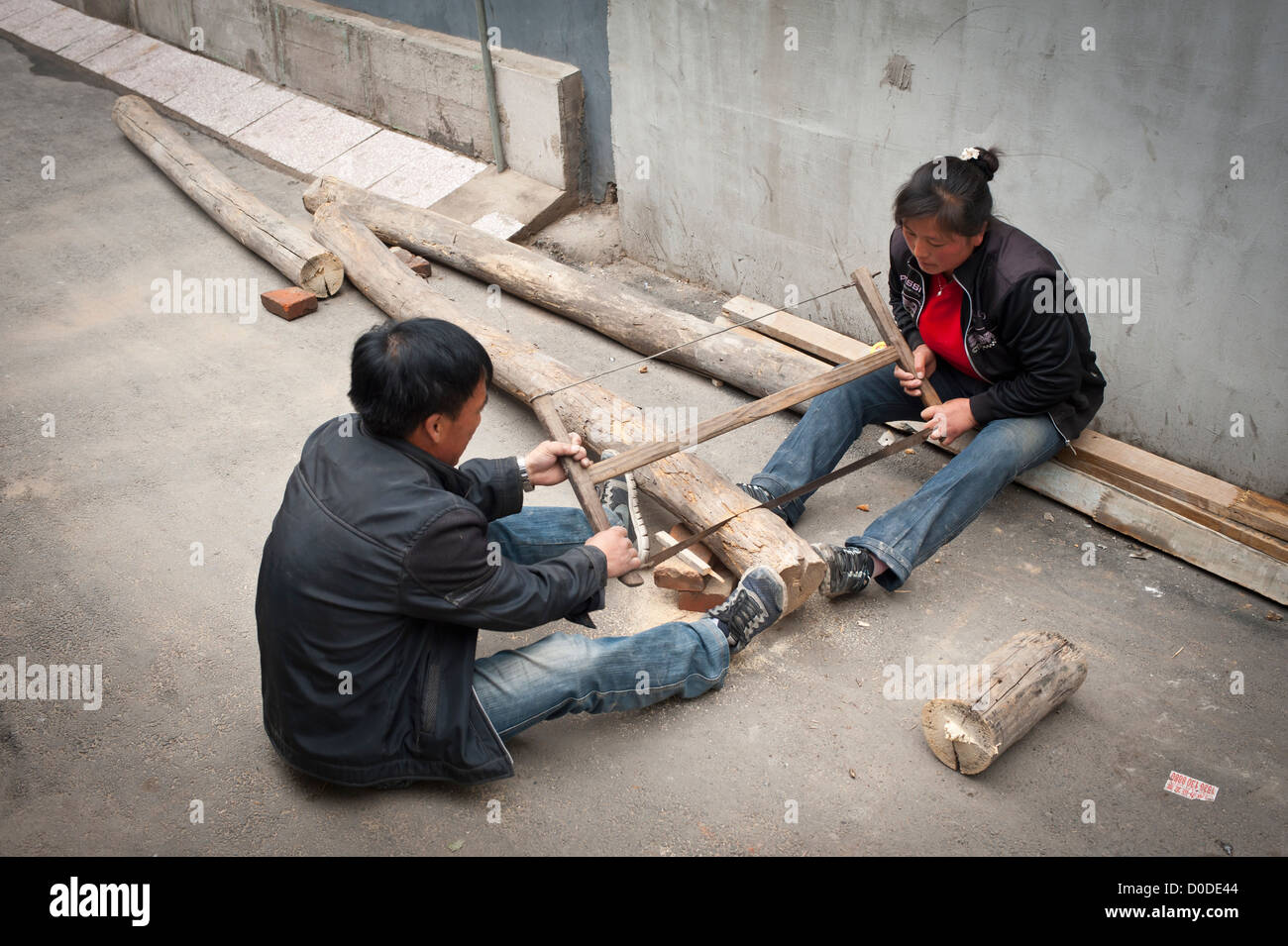 Chinese man and woman use a handsaw to cut a log Stock Photo