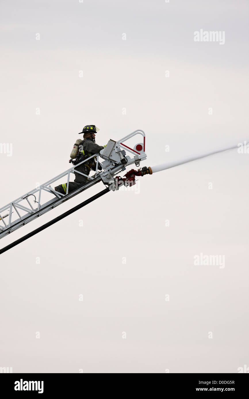 Firefighter spraying water on building fire from end of a ladder, using a water cannon Stock
