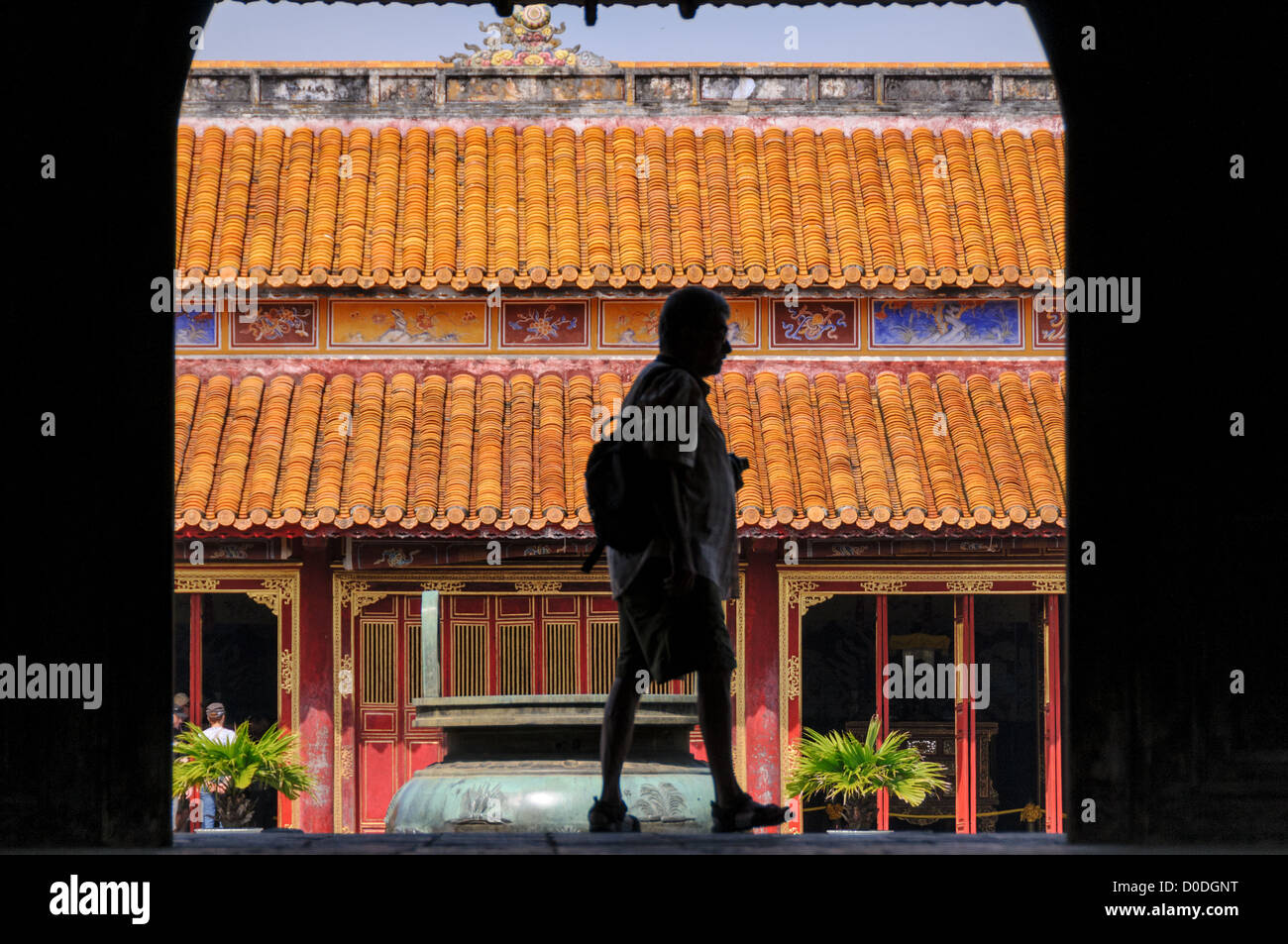 HUE, Vietnam - A tourist is silhouetted against To Mieu Temple at the Imperial City in Hue, Vietnam. A self-enclosed and fortified palace, the complex includes the Purple Forbidden City, which was the inner sanctum of the imperial household, as well as temples, courtyards, gardens, and other buildings. Much of the Imperial City was damaged or destroyed during the Vietnam War. It is now designated as a UNESCO World Heritage site. Stock Photo
