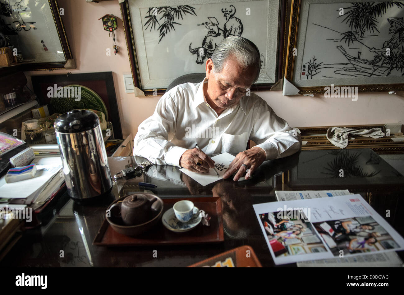 HUE, Vietnam - Local artisan Kinh Van Le, a master of traditional Hue silk embroidery, writes at his desk on his store in Hue, Vietnam. Some of his work hangs on the wall in the background. Stock Photo