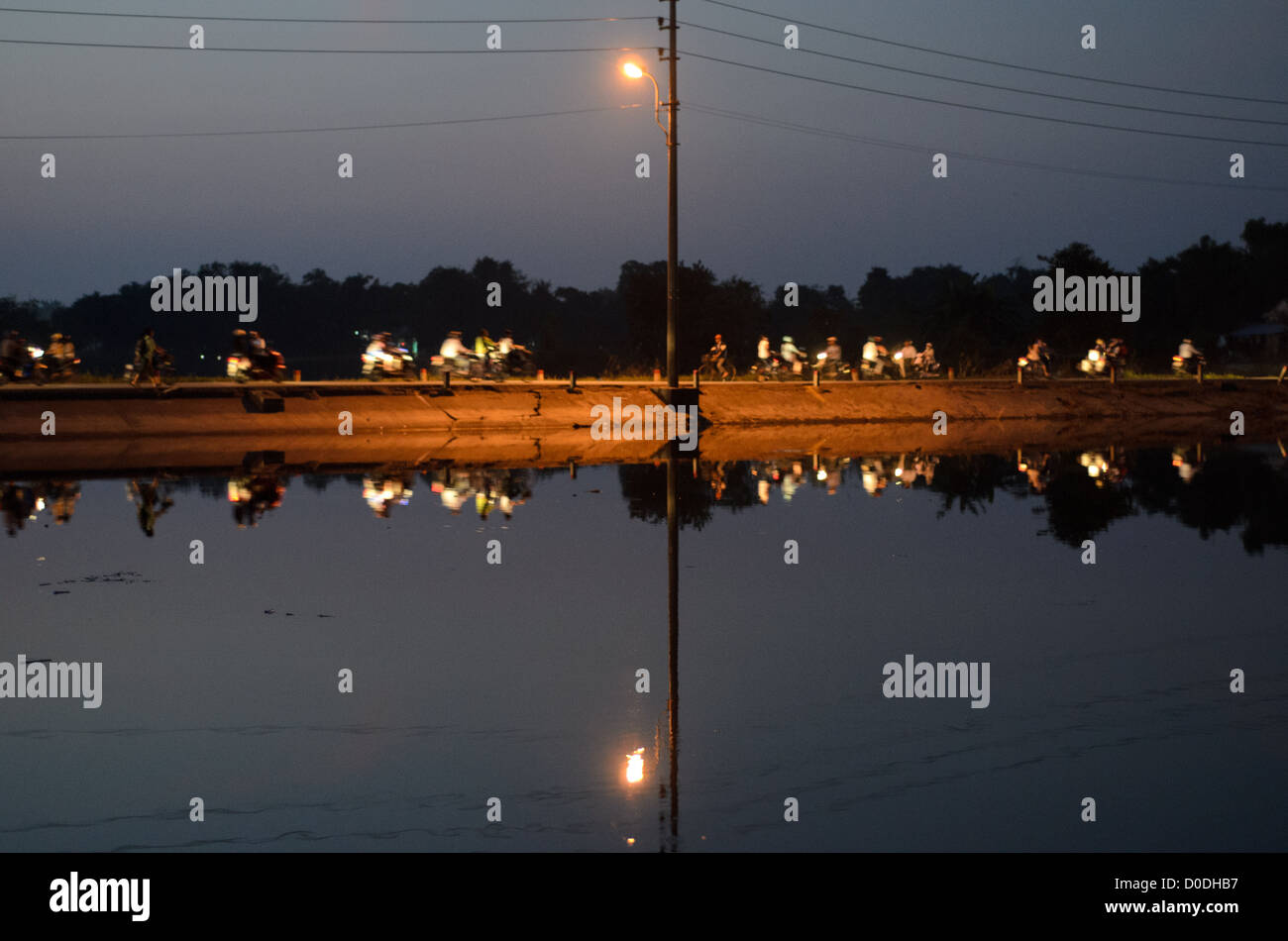 HUE, Vietnam - Evening traffic rushes over a thin embankment of the Perfume River in Hue, Vietnam, reflected on the glassy water. Stock Photo