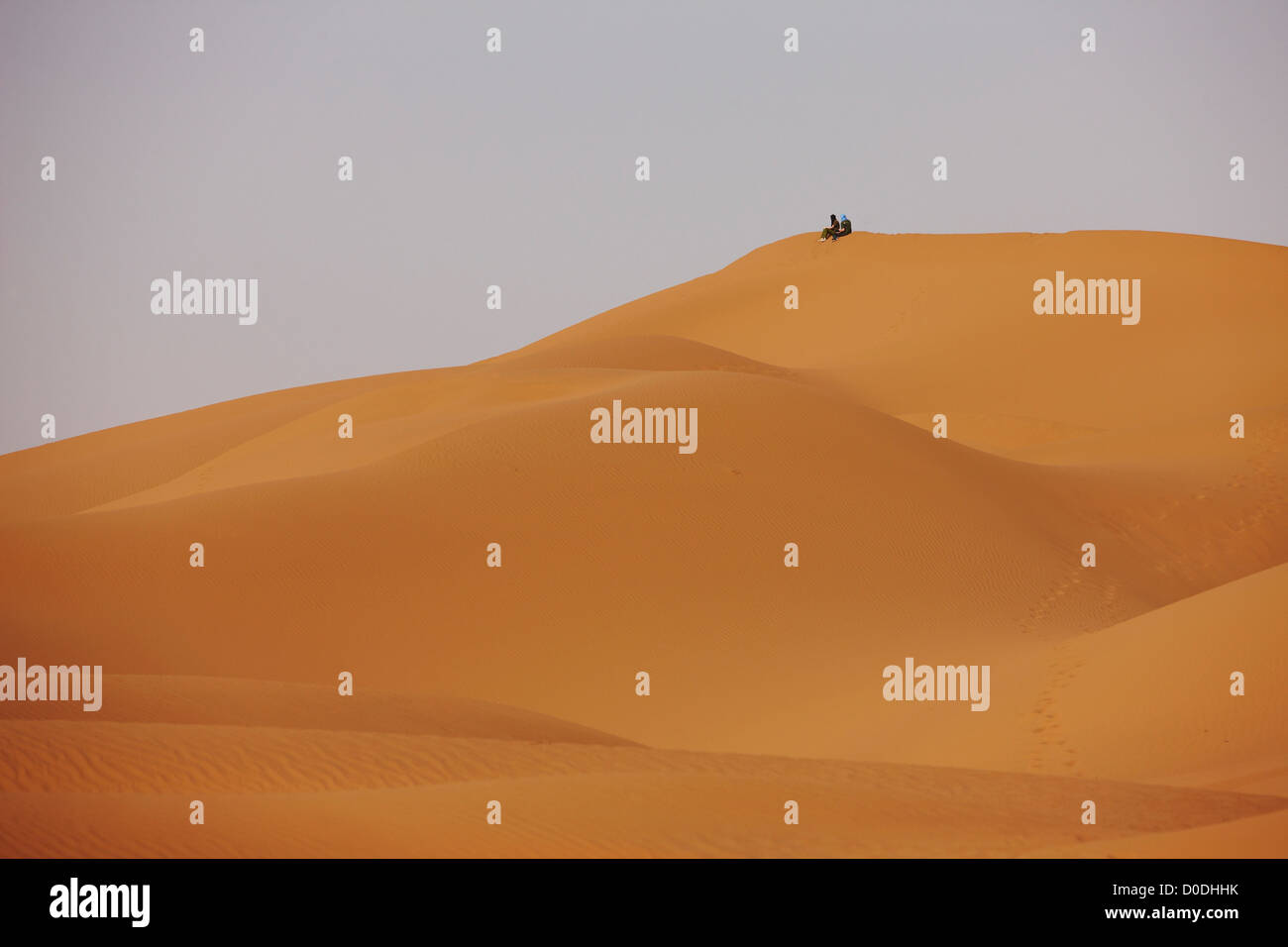 two people atop large sand dune in Erg Chegaga, interior Sahara Desert, Morocco Stock Photo