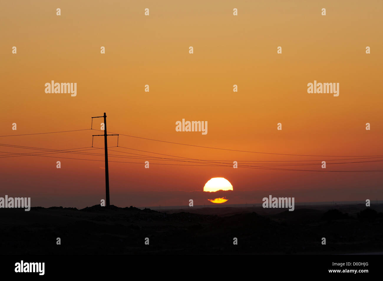 Setting sun silhouettes high voltage power lines and power line pole, near Laayoune, Western Sahara, North Africa Stock Photo