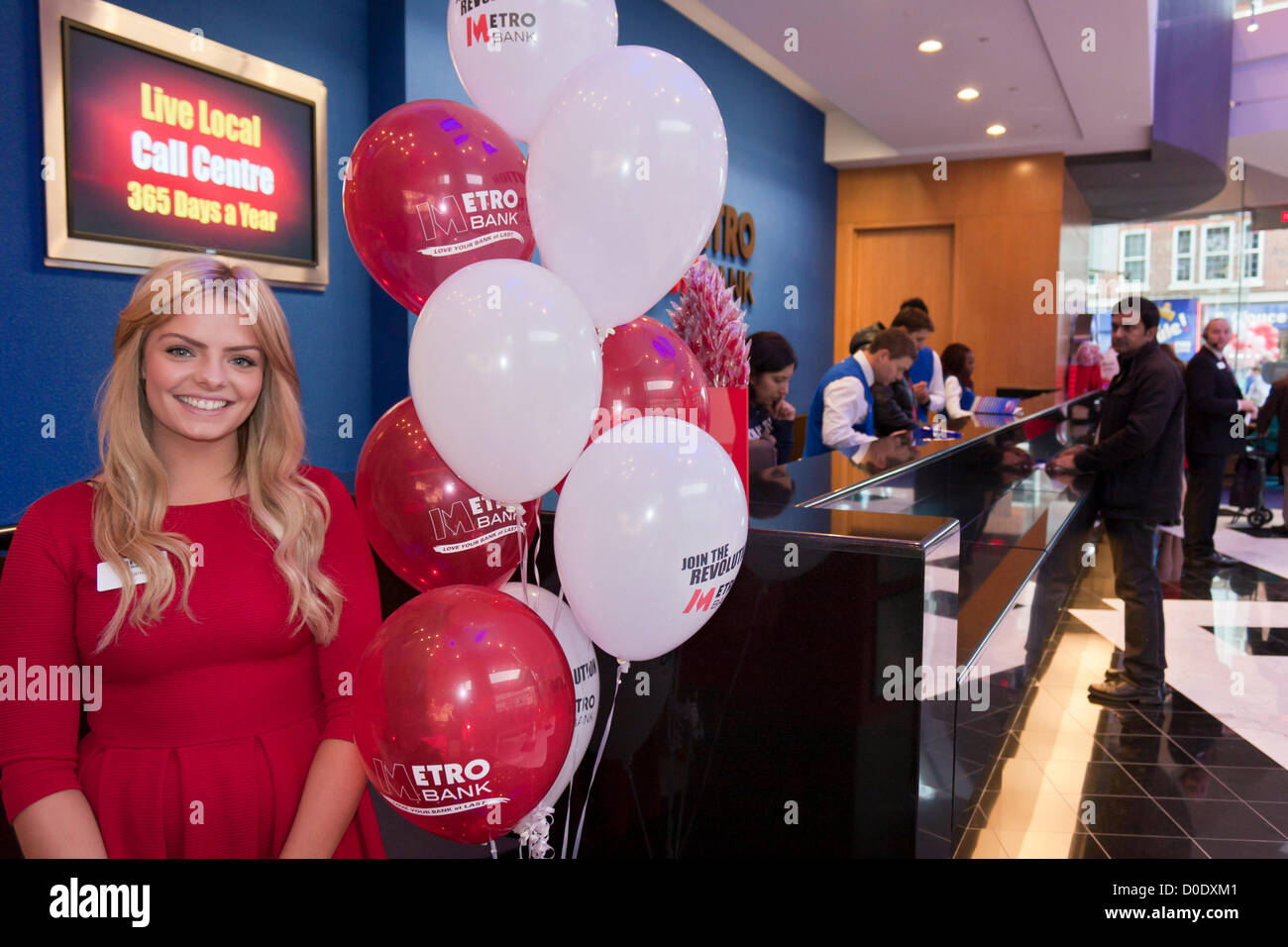 Stefanie welcomes customers at the new branch of Metro Bank in Reading, Berkshire on November 23rd 2012; cashiers welcome new customers in the background. Stock Photo