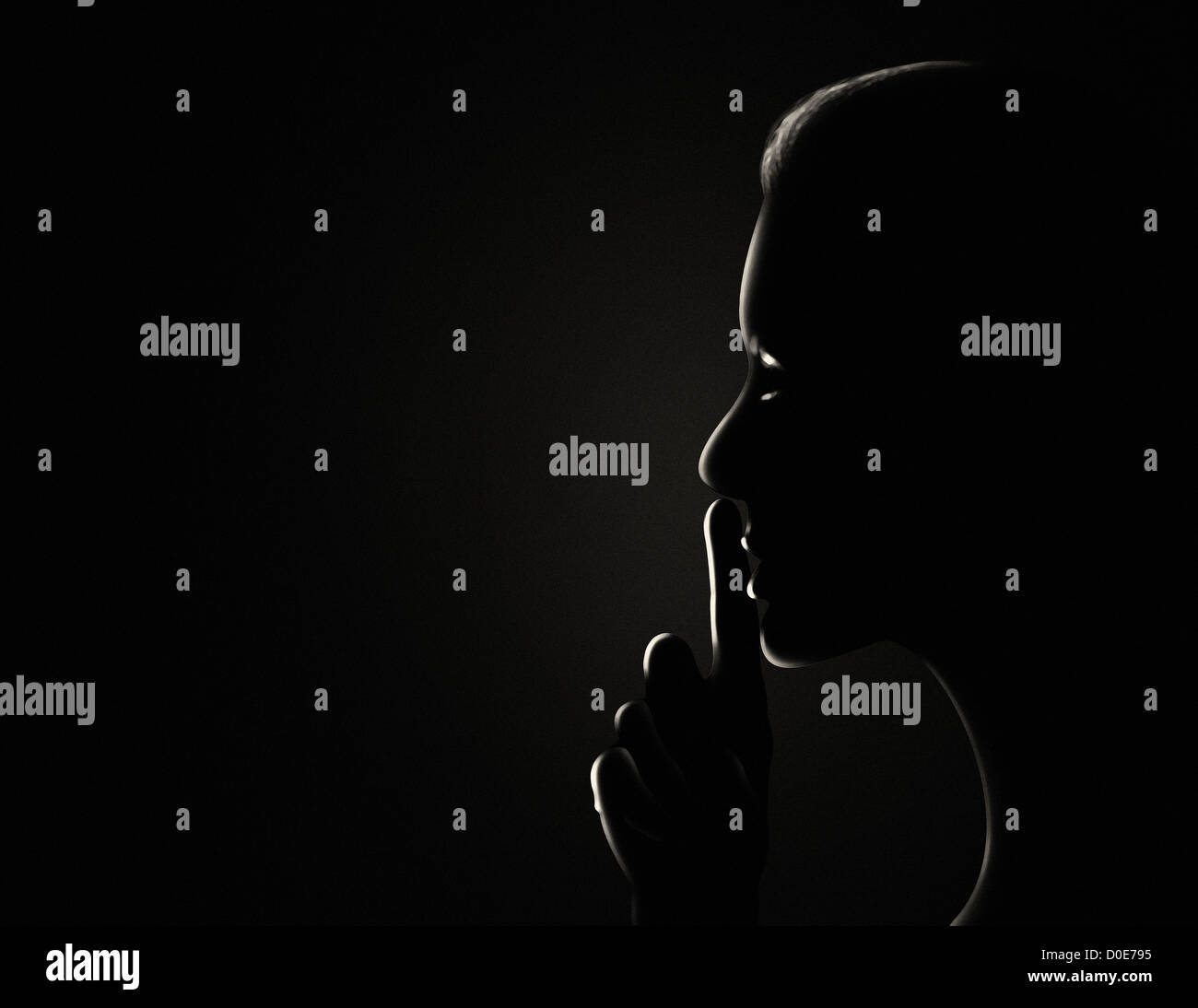 Woman in the dark with her finger to her lips gesturing silence. Stock Photo