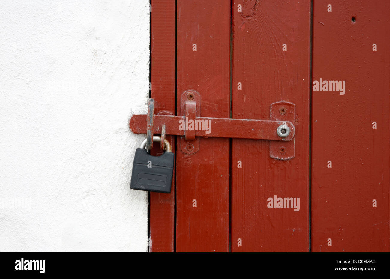 Whitewashed fishing shed with red wooden door locked with bolt and padlock. Stock Photo