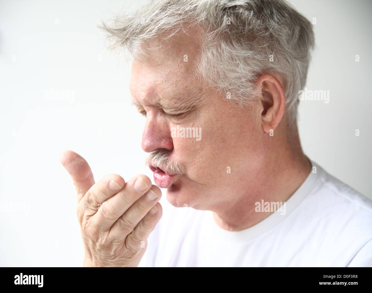 senior man sneezes into his hand Stock Photo