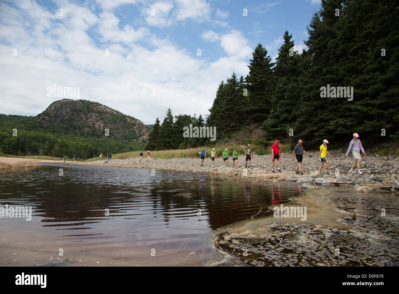Hikers wearing colorful outdoor gear walking around a lake in Acadia