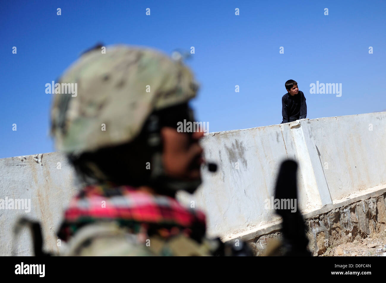 A local Afghan boy watches US soldiers guard a compound September 26, 2012 during a mission to Pur Chaman district, Farah province, Afghanistan, Sept. 26. The mission marks the first time coalition forces have been to the Pur Chaman district in over a year. Stock Photo