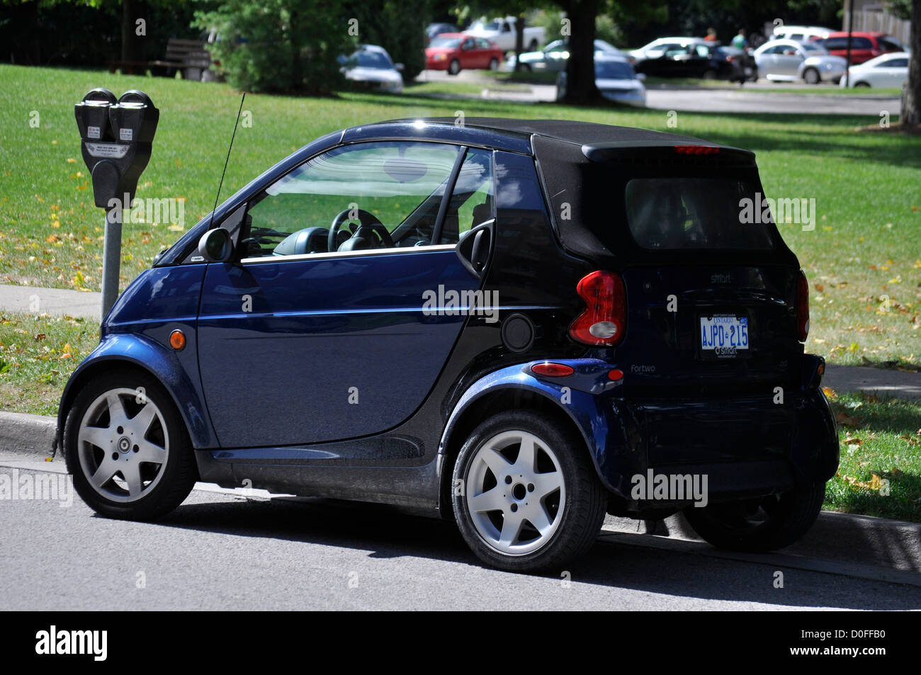 A very small Smart car parked at a street meter in Ontario, Canada.  Time limited. Coin operated. Residential area. Conventional. Not electric. Stock Photo