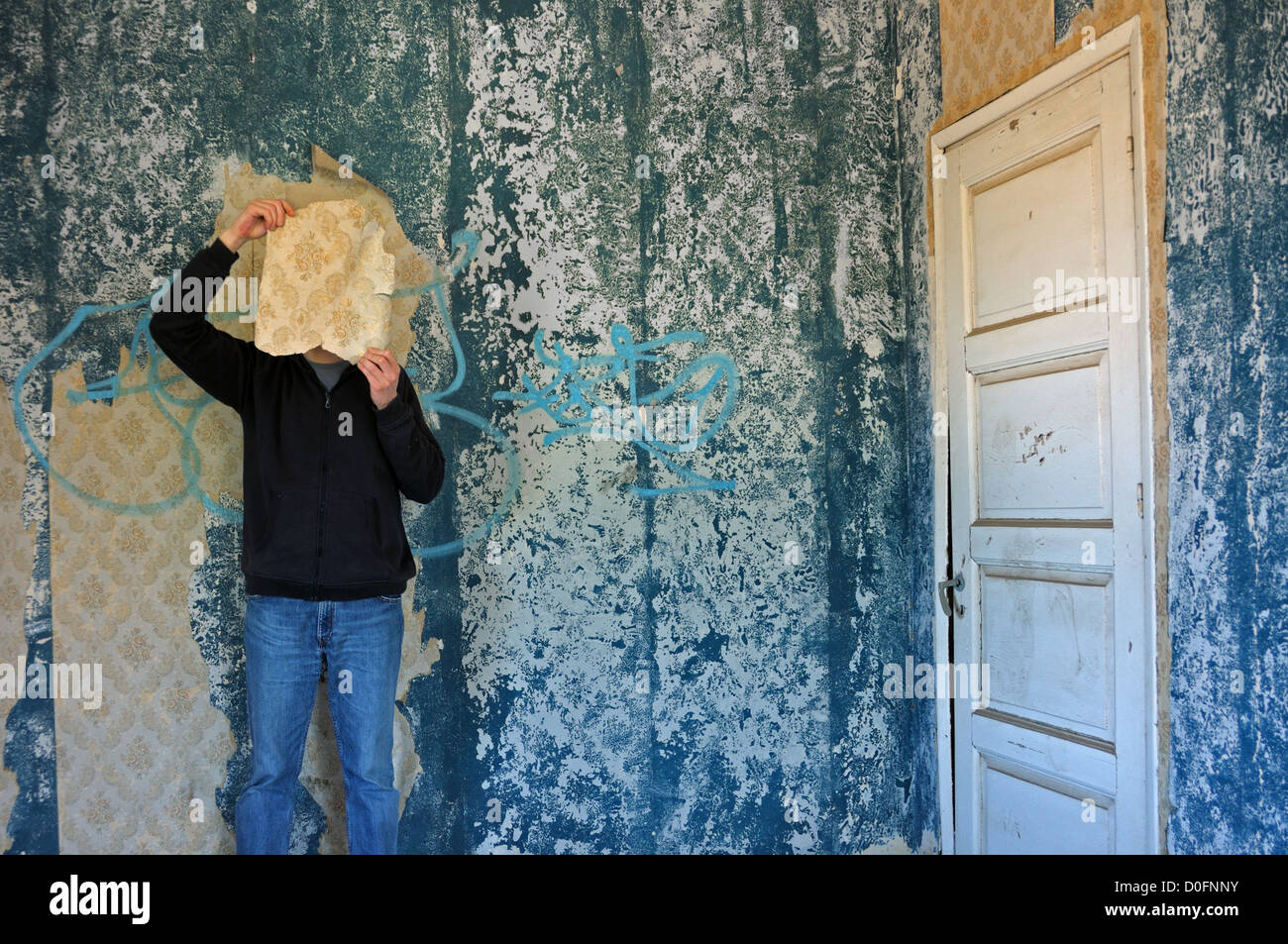 Man with torn wallpaper shred in decayed blue room abandoned house interior. Stock Photo