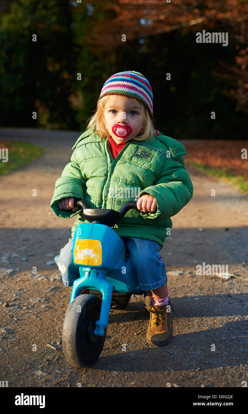 One year old girl riding toddler plastic trike (tricycle) in autumn