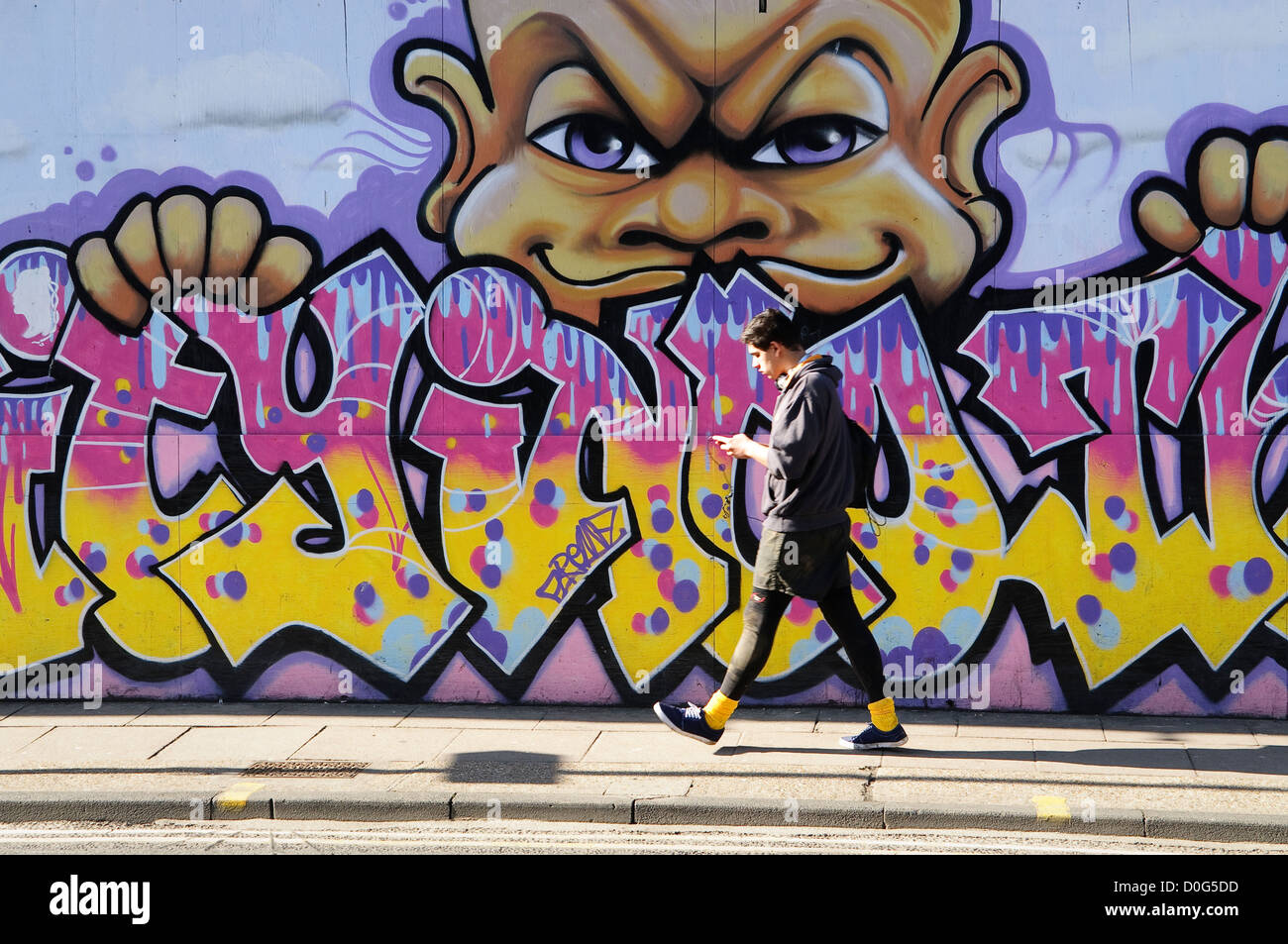 Young man walking down the street, along painted wall, Ipswich, Suffolk, UK. Stock Photo