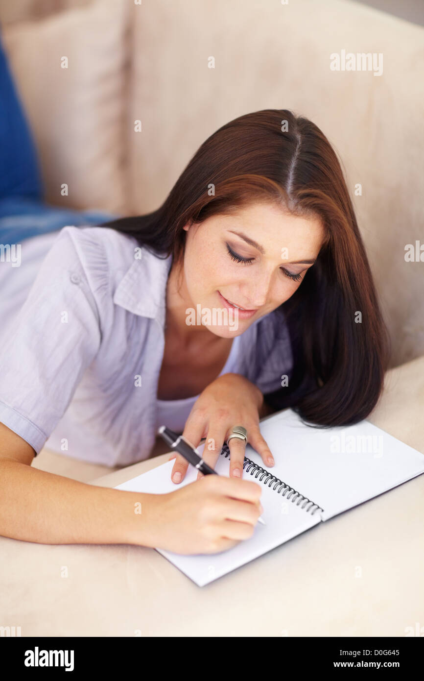 An attractive young woman lying on a couch writing in a book Stock ...