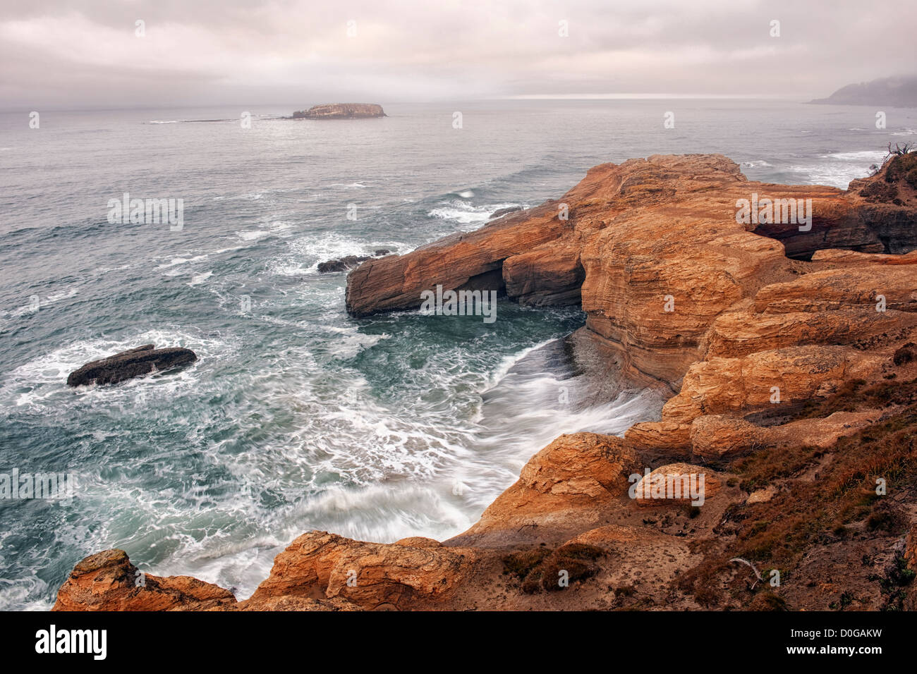 Morning fog lifts revealing the sandstone cliffs of Oregon’s Devil’s Punchbowl State Park and offshore Gull Island. Stock Photo