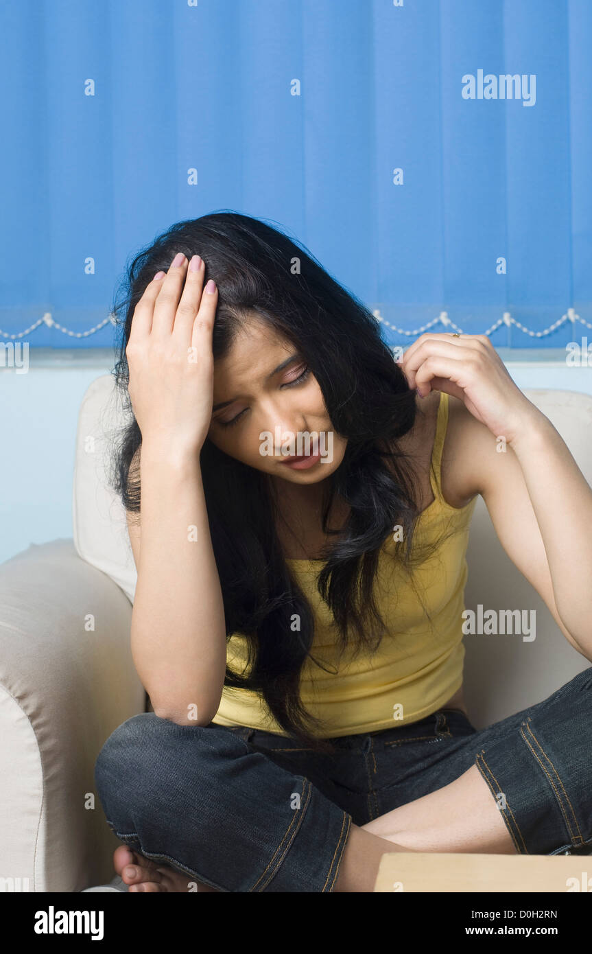Young woman sitting on a couch with her head in her hand Stock Photo