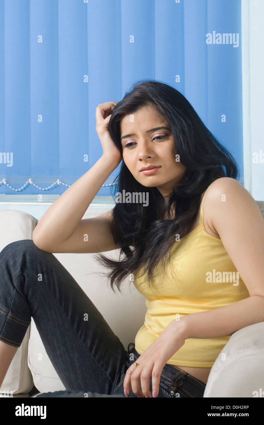 Young woman sitting on a couch with her head in her hand Stock Photo