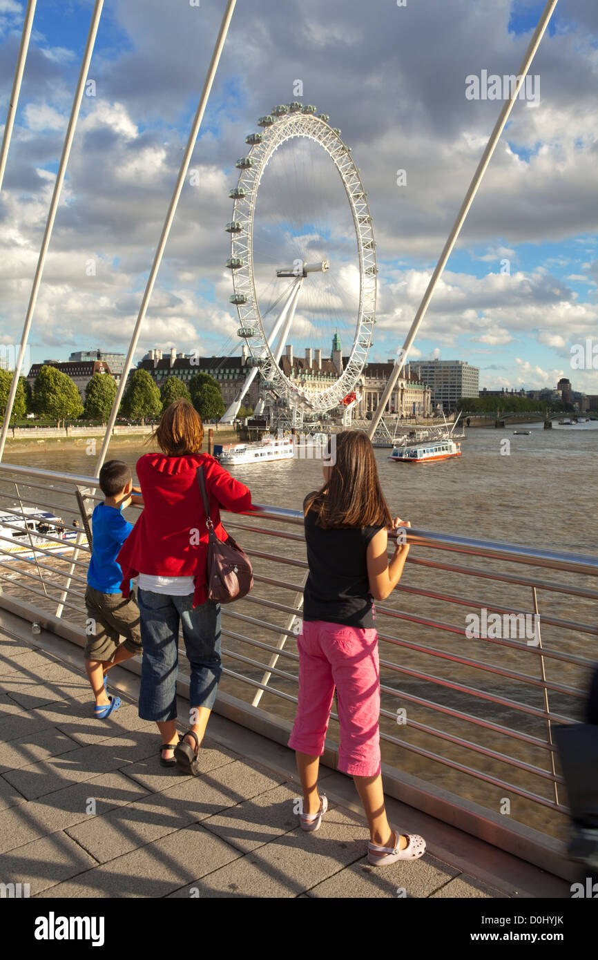 A mother and her children enjoy the view of the London Eye from the Hungerford Bridge over the river Thames. Stock Photo