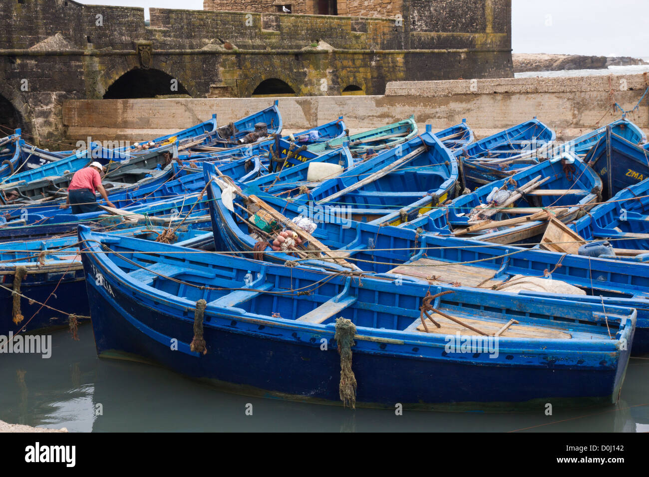 Man working in mass of Blue fishing boats in  Essaouira harbour Stock Photo